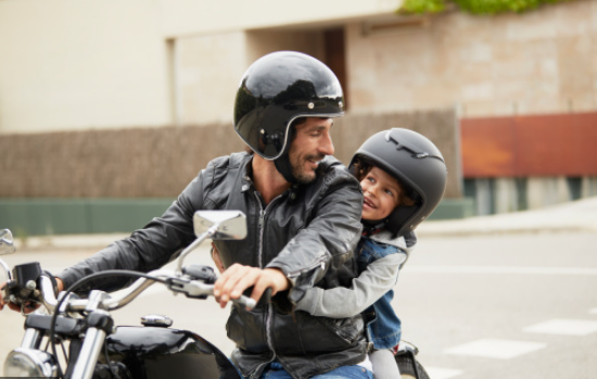 Dois homens numa moto com fatos e capacetes pretos numa rua urbana