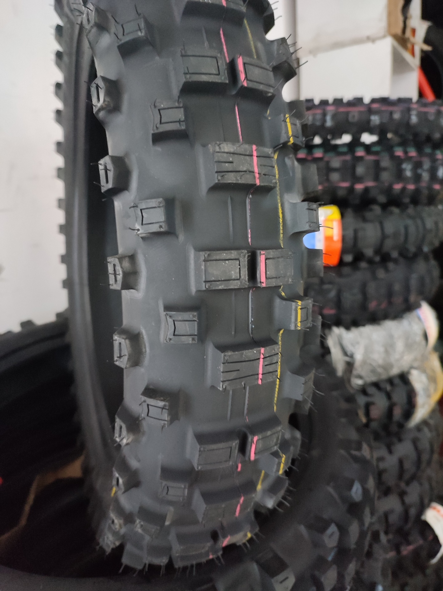 Pneu todo-o-terreno preto com padrão em relevo e linhas vermelhas e amarelas