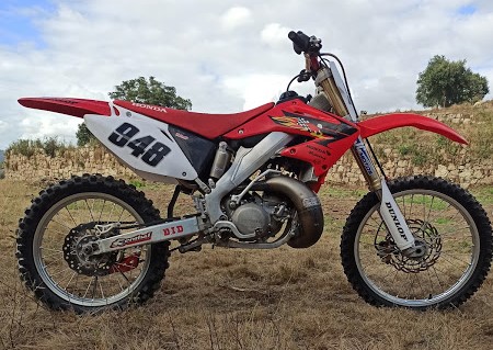 Motocross vermelho e branco com número 848 em campo seco