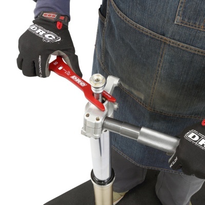 Pessoa a usar luvas pretas DRC a ajustar ferramenta vermelha numa peça metálica prateada com roupa de trabalho.