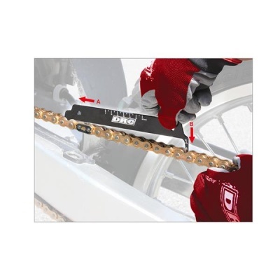 Corrente dourada de bicicleta a ser medida com régua preta com etiqueta DRC e mãos com luvas vermelhas