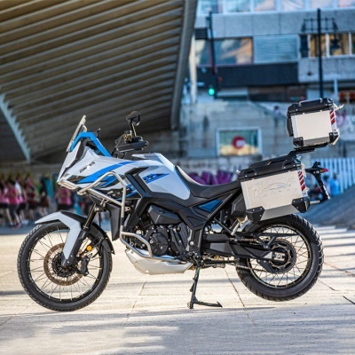 Motociclo de aventura com malas metálicas estacionado em calçada urbana