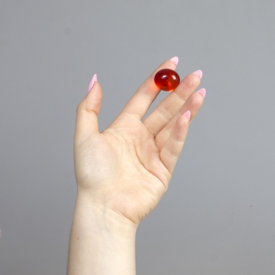 Mão feminina segurando cápsula vermelha translúcida