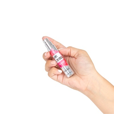 Frasco metálico prateado pequeno com spray e rótulo colorido numa mão