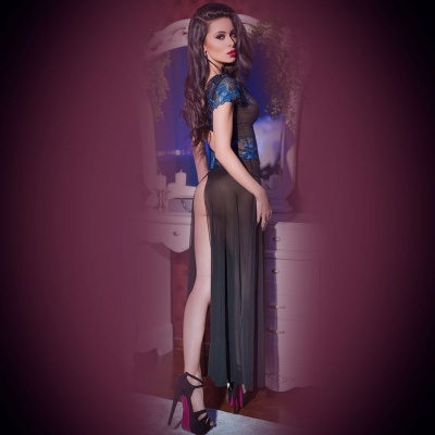 Mulher com vestido transparente preto com detalhes azuis e salto alto preto, frente a móvel branco com espelho oval