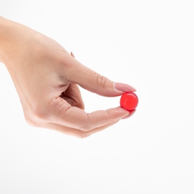 Mão feminina segurando um pequeno objeto redondo vermelho