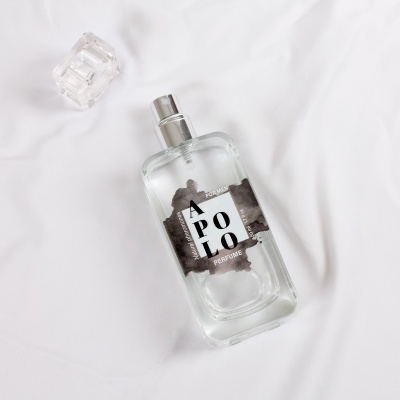 Frasco de perfume transparente com etiqueta APOLLO sobre tecido branco