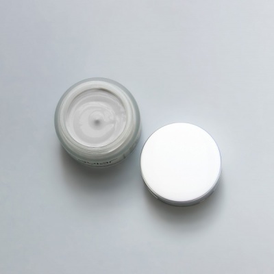 Frasco aberto de creme branco com tampa branca ao lado