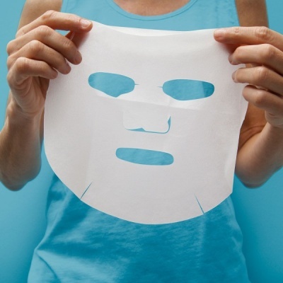 Máscara facial branca de tecido fino com recortes segura por pessoa com camisola azul