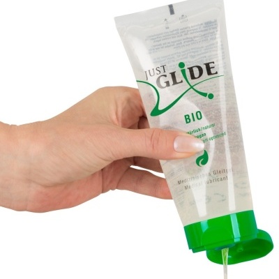 Mão segurando tubo transparente de lubrificante Just Glide Bio com tampa verde