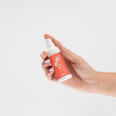 Frasco de spray branco com rótulo vermelho segurado por uma mão com unhas cor-de-rosa claro