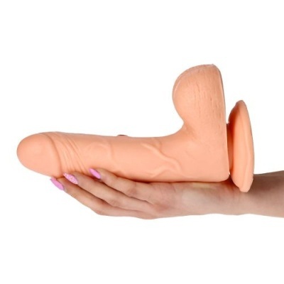 Dildo cor pele com textura realista e base circular segurado por mão com unhas cor rosa claro.