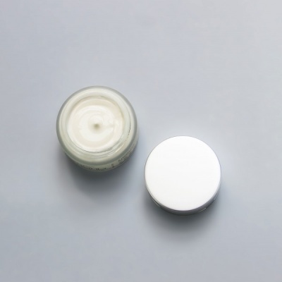 Frasco aberto de creme branco com tampa branca ao lado