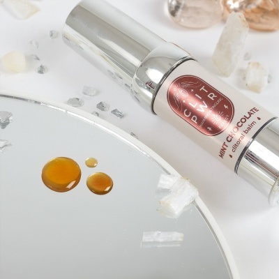 Frasco prateado de estora-balm White Chocolate com cristais e gotas castanhas sobre espelho