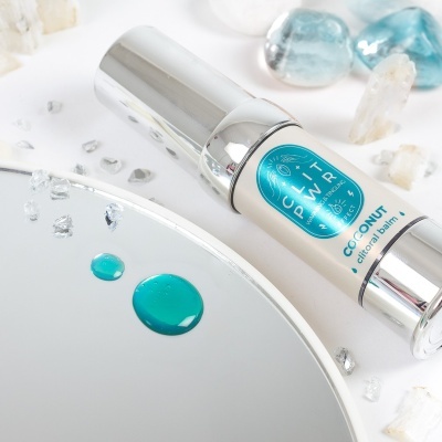 bálsamo cítrico em frasco prateado com rótulo azul e branco sobre espelho com gotas azuis e pedras