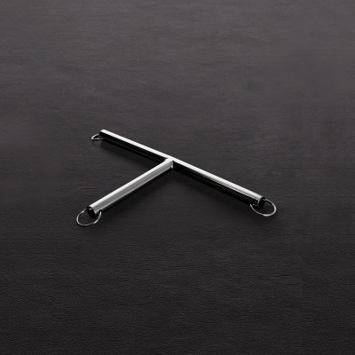 Ferramenta metálica em forma de T com anéis nas extremidades sobre superfície preta