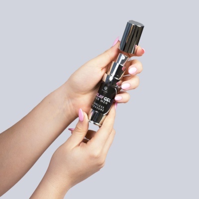 Frasco de gel para homens incolor com rótulo preto e tampa prateada segurado por mãos femininas com unhas cor de rosa