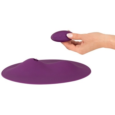 Base oval de silicone roxo com superfície ondulada e controlo remoto oval da mesma cor segurado por mão