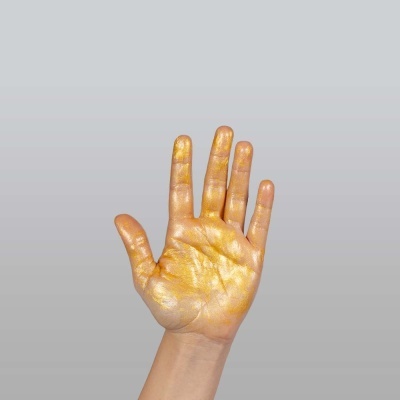 Mão pintada de dourado contra fundo cinzento