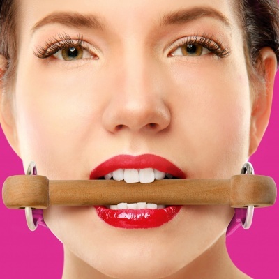 Rosto feminino com batom vermelho a segurar objeto de madeira entre os dentes