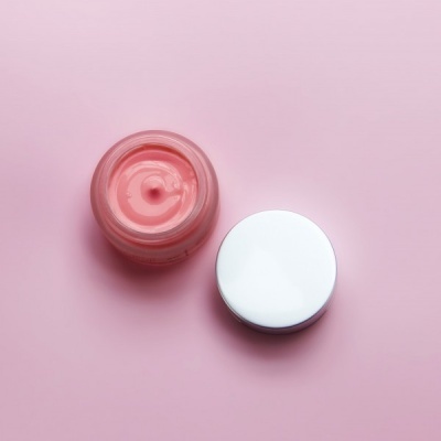 Frasco aberto com creme rosa e tampa branca sobre superfície rosa