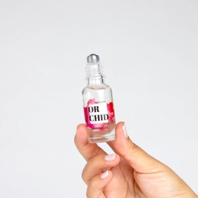 Frasco de óleo de perfume transparente com etiqueta 'ORCHID PERFUME OIL' na mão