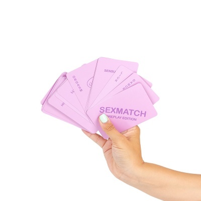 Cartas rosas 'SEXMATCH FOREPLAY EDITION' numa mão com unhas verdes