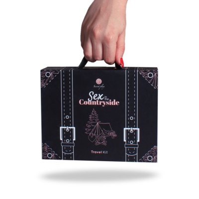 Mala preta 'Sex the Countryside Travel Kit' com alça preta e ilustrações brancas e rosa, segurada por mão com unhas vermelhas