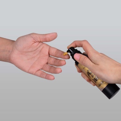 Mãos segurando frasco e aplicando líquido dourado com fundo cinzento