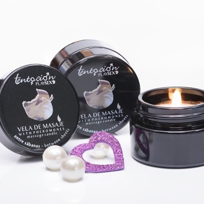 Velas de massagem TENTACION BY LUXERY em frascos pretos, uma vela acesa, coração decorativo roxo e pérolas brancas