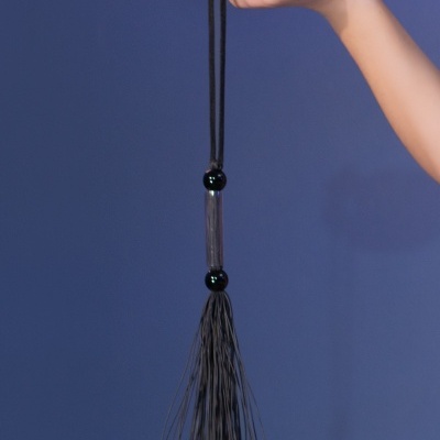 Chicote pequeno preto pendurado numa mão com fundo azul-lilás
