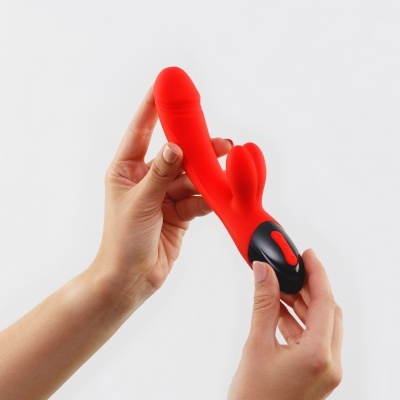 Vibrador vermelho anatómico com base preta e botão vermelho segurado por mãos