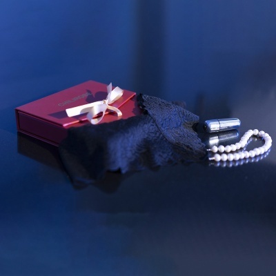 Acessórios femininos sobre superfície espelhada com caixa vermelha e laço, batom, pulseira de pérolas e luva de renda preta