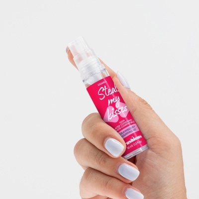 Frasco vermelho e branco de spray segurado por mão com unhas lilás claro