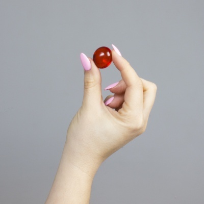 Mão segurando cápsula vermelha translúcida com unhas rosas