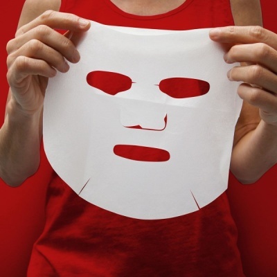 Máscara facial branca de tecido com recortes segurada por pessoa com camisa vermelha