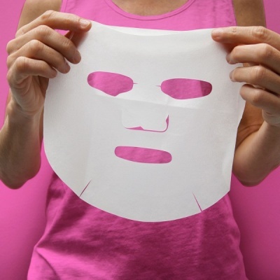 Máscara facial branca de papel segurada por pessoa com camisa rosa.