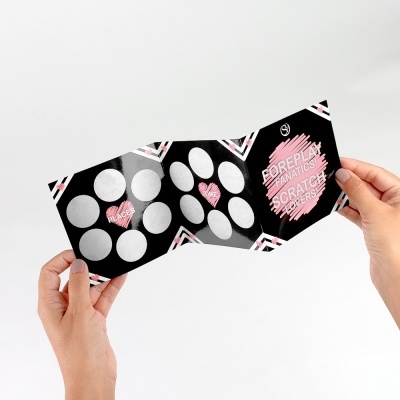 Cartão de jogo com círculos prateados, texto rosa e branco em fundo preto segurado por duas mãos