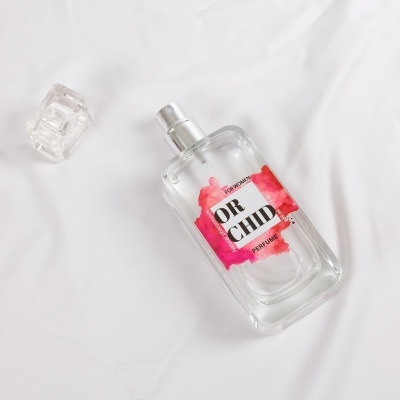 Frasco de perfume transparente com rótulo colorido e tampa ao lado