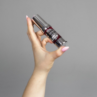 Mão segurando batom de estojo metálico prateado com tampa transparente e texto LIQUID LIP TATTOO