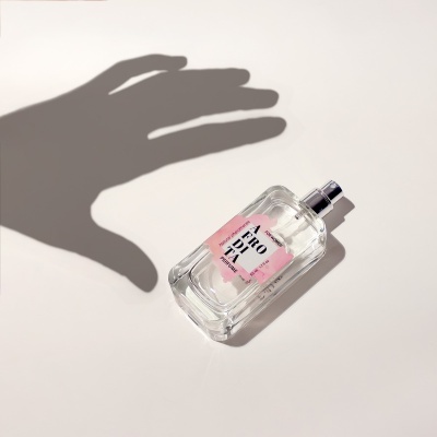 Frasco de perfume transparente com rótulo cor-de-rosa e sombra de uma mão ao fundo