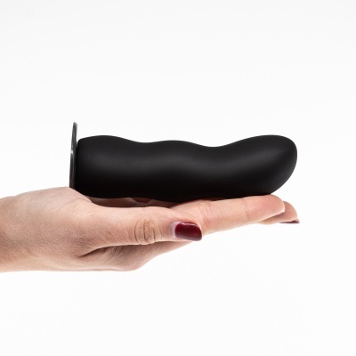 Plug anal preto de silicone numa mão com unhas vinho fundo branco