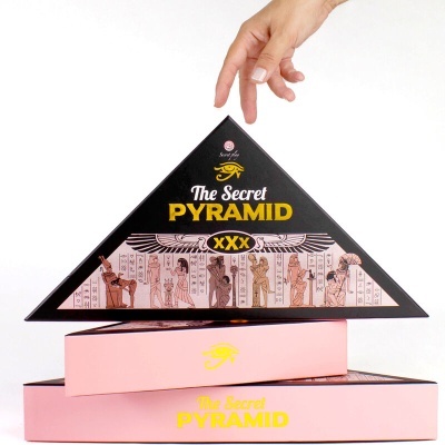 Caixa triangular preta com texto amarelo e ilustrações egípcias apoiada em caixas cor de rosa