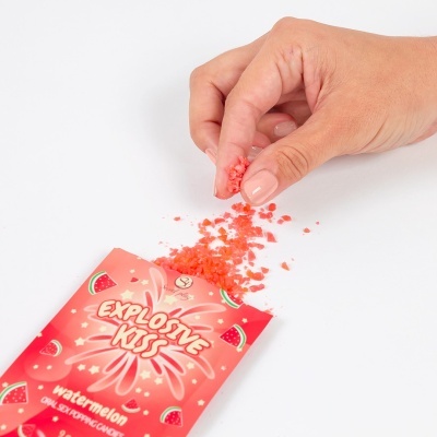 Pacote vermelho de Explosive Kiss aberto com grânulos vermelhos e mão a pegar os grânulos