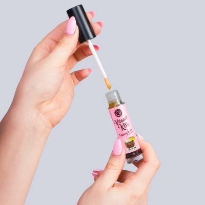 Frasco pequeno de óleo labial com aplicador branco e tampa preta em mãos femininas