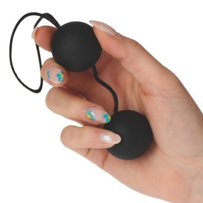 Bolas Ben Wa pretas ligadas por cordão seguradas por mãos femininas com unhas decoradas.