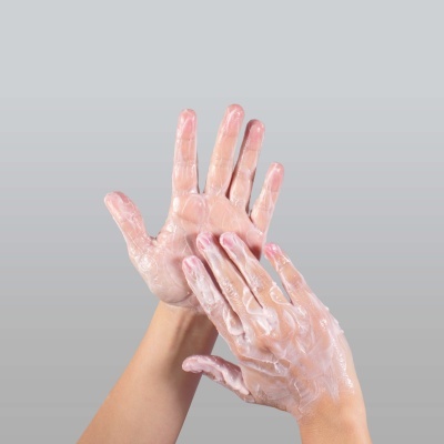 Mãos com espuma de sabão branca em fundo cinzento