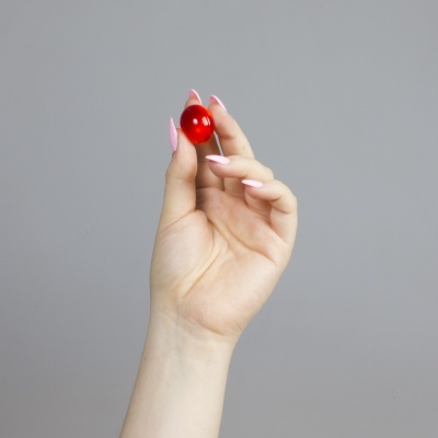 Mão feminina segurando esfera vermelha sobre fundo cinzento