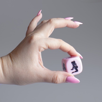 Mão segurando dado rosa com figura preta em fundo cinza