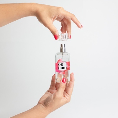 Frasco transparente com etiqueta 'OR CHID' segurado por mãos com unhas vermelhas